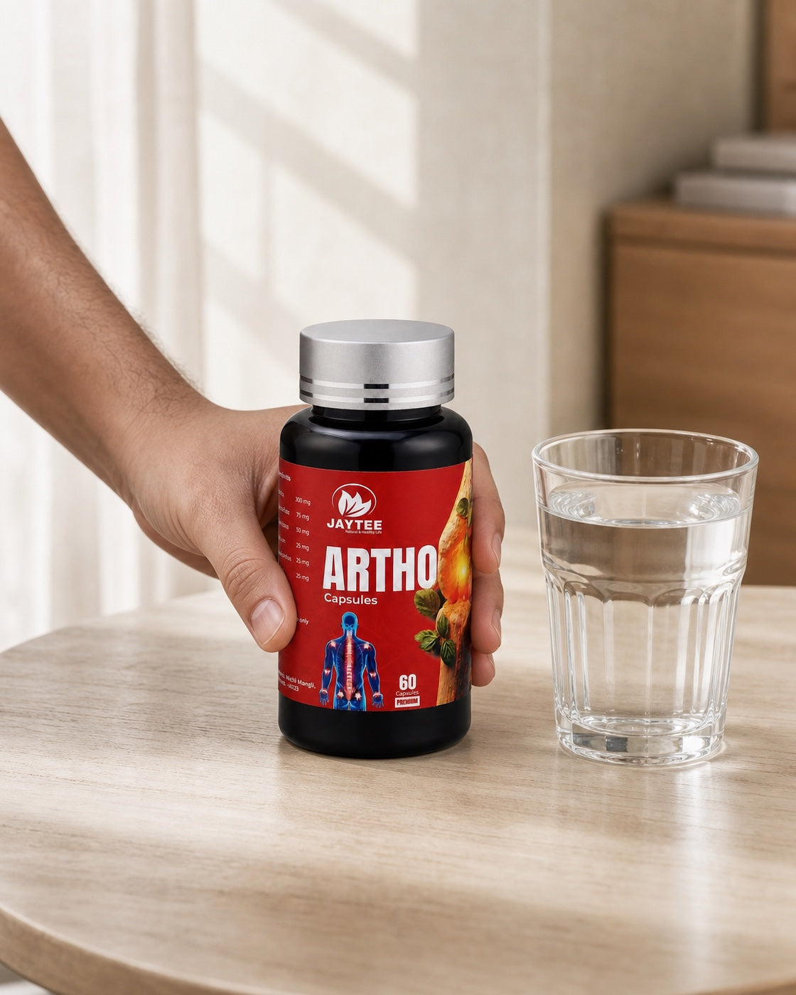 Adult hand placing a closed Arthro Capsules bottle beside a glass of water