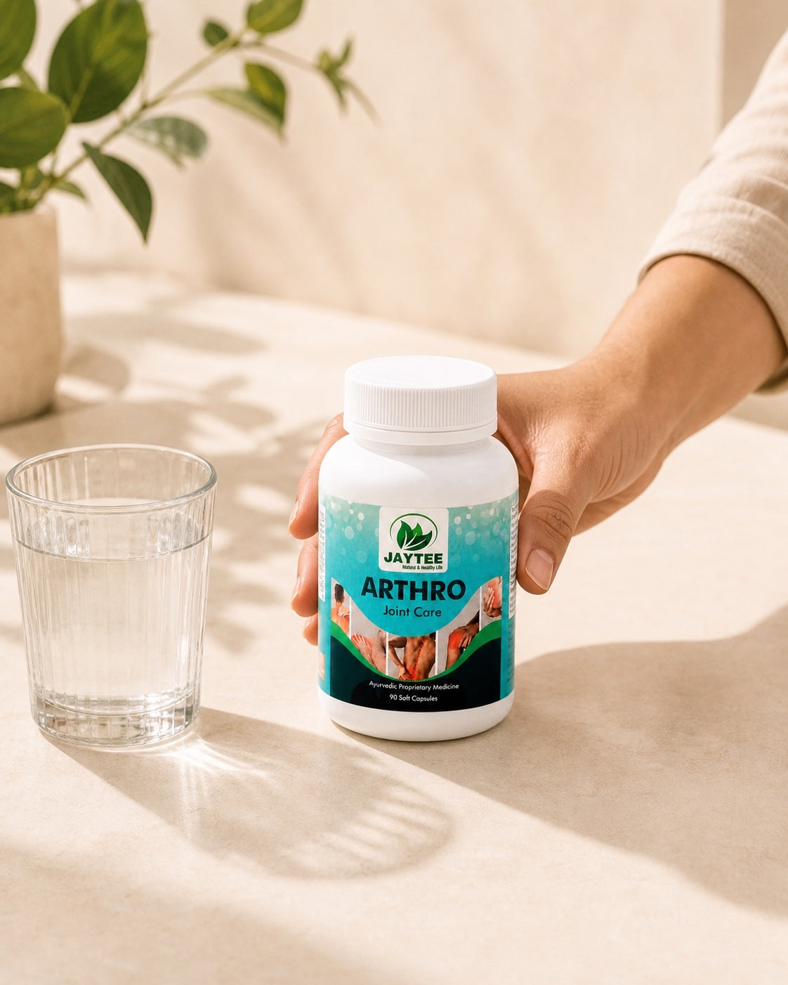 Adult hand placing a closed Arthro Joint Care bottle beside a glass of warm water